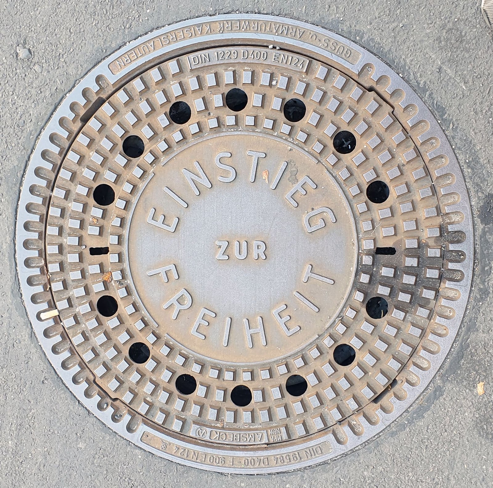 Round cast-iron manhole cover in the pavement with the raised words 'Einstieg zur Freiheit'