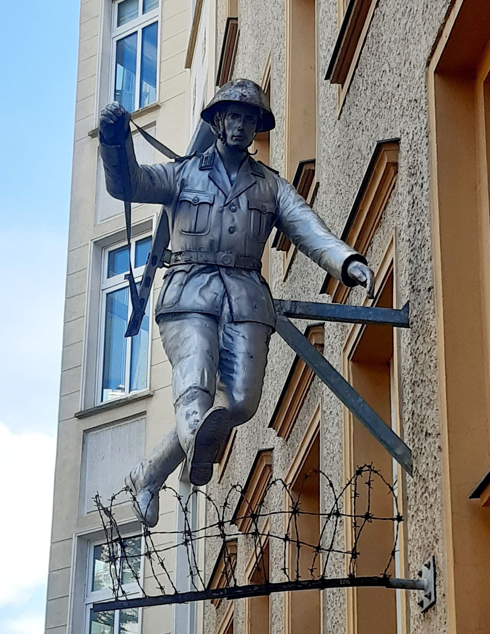 Close view of a metal sculpture of a helmeted soldier in mid-leap over barbed wire.