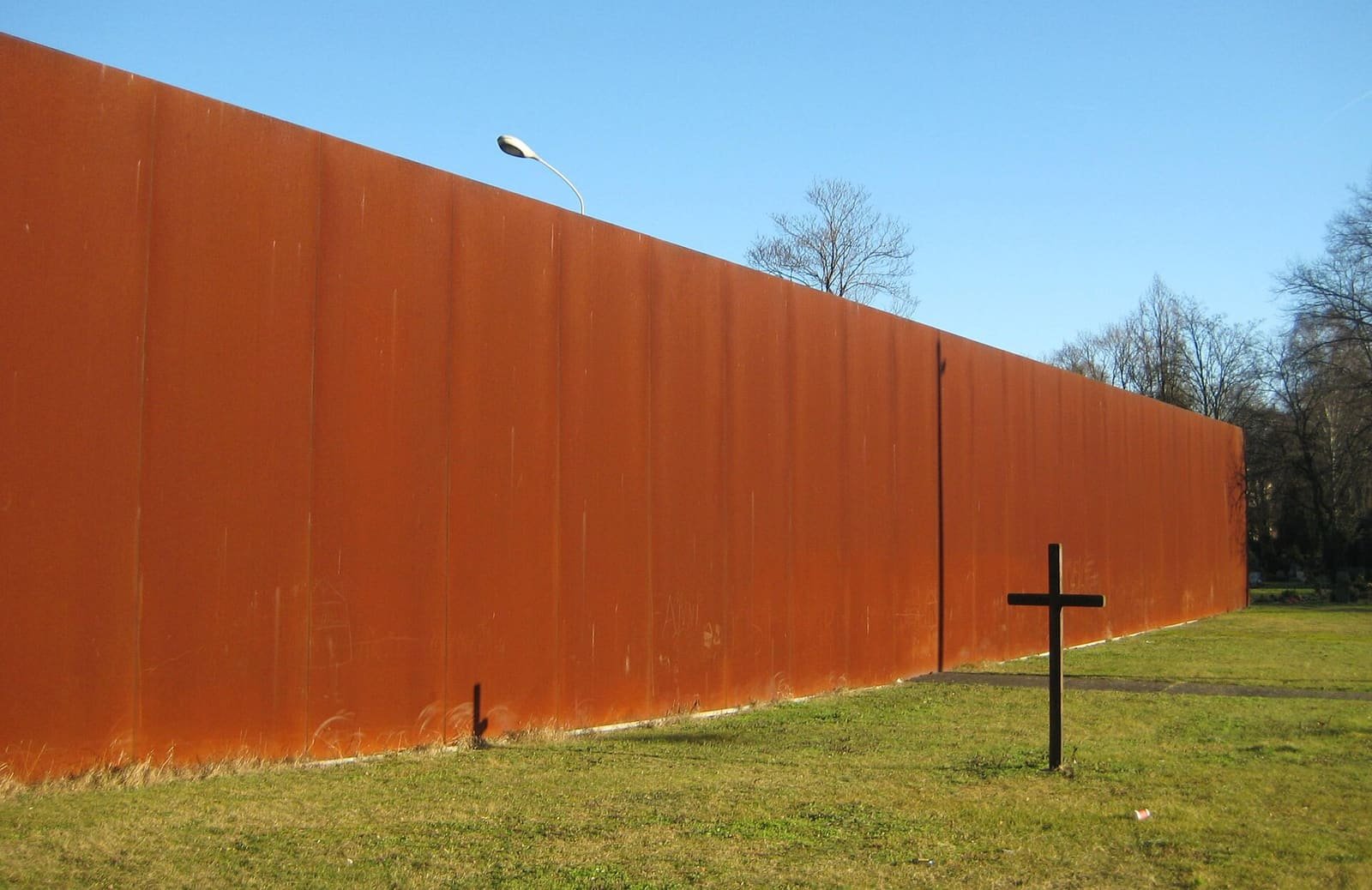 A grey concrete wall seen from a cemetery, with bare winter trees