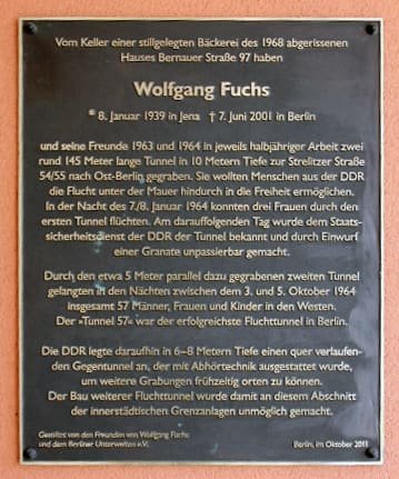 Dark bronze-coloured plaque with white German text headed 'Wolfgang Fuchs', fixed to a reddish wall.