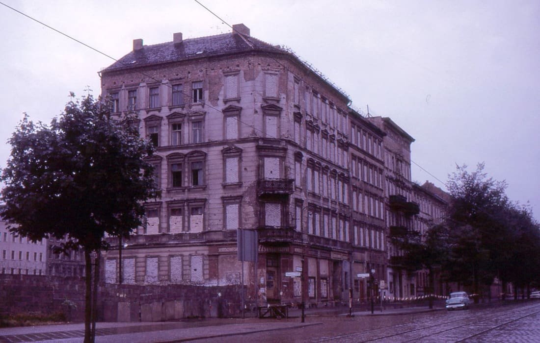 Historical photograph of a corner apartment building and a row of houses on Bernauer Straße with bricked-up windows