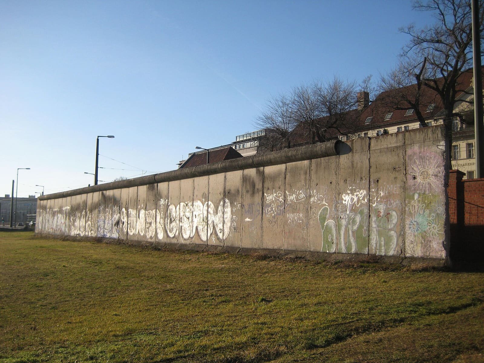 A long grey concrete wall section seen across the grounds of a cemetery, with bare winter trees