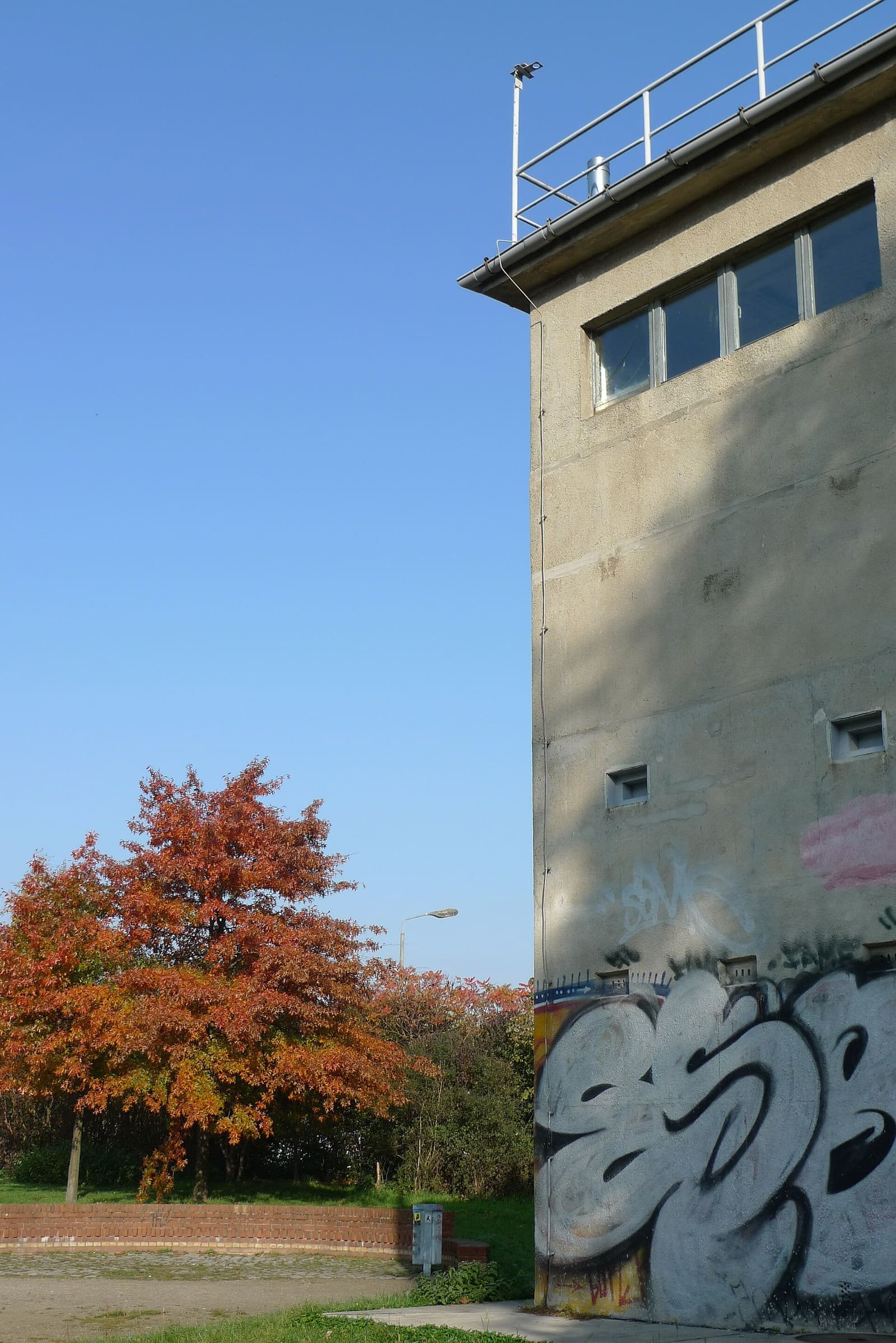 A square concrete former border watchtower among autumn trees in a park.