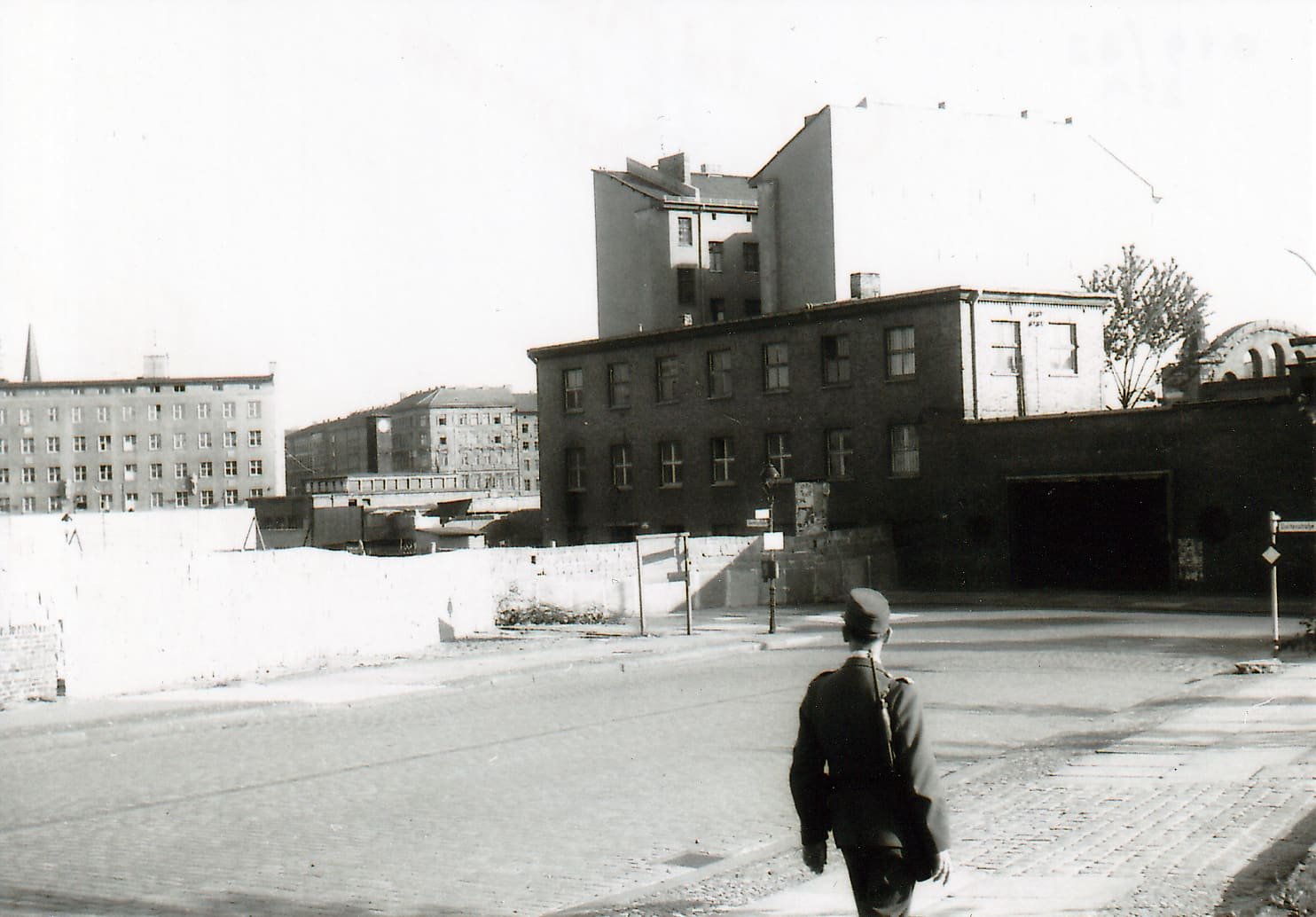 Black-and-white street scene with a wall across the road, a West Berlin policeman in the foreground and a closed station entrance