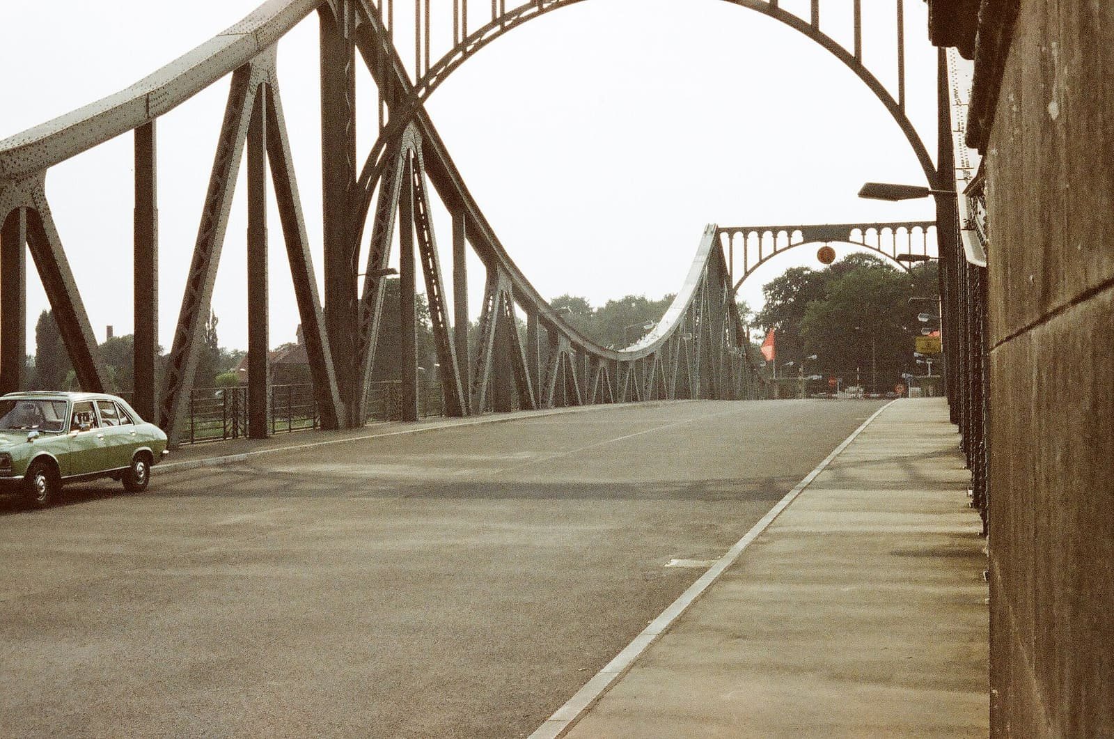 Colour photo of the green steel arch bridge with an empty roadway, a single car parked at the side.
