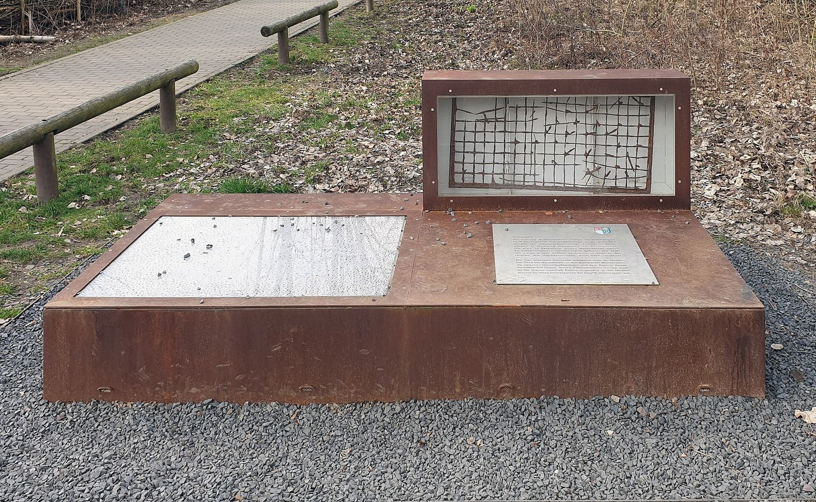 An outdoor memorial displaying a section of spiked border barrier beside a residential street