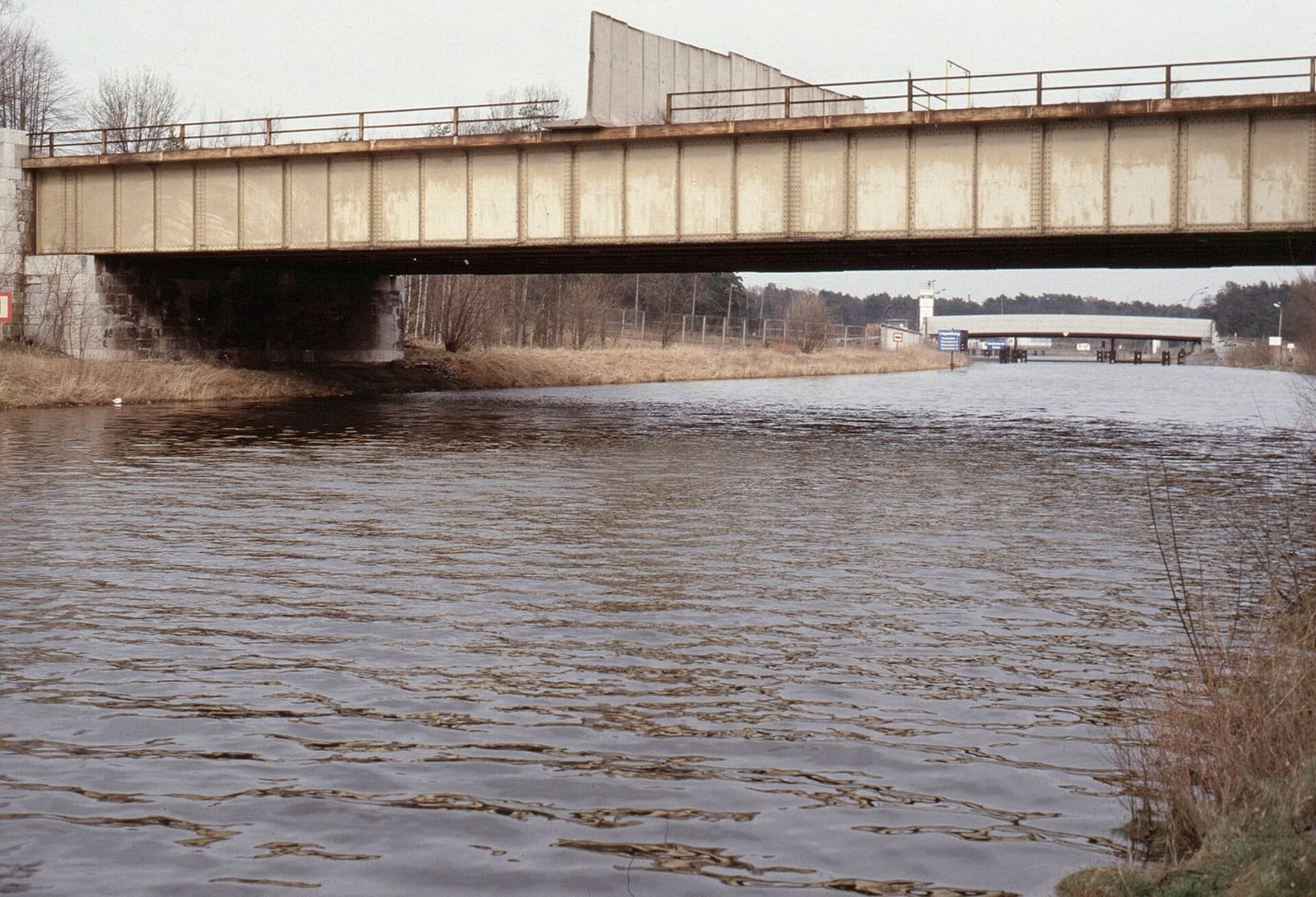 A canal with bridges crossing it; a section of wall stands across the nearer bridge.