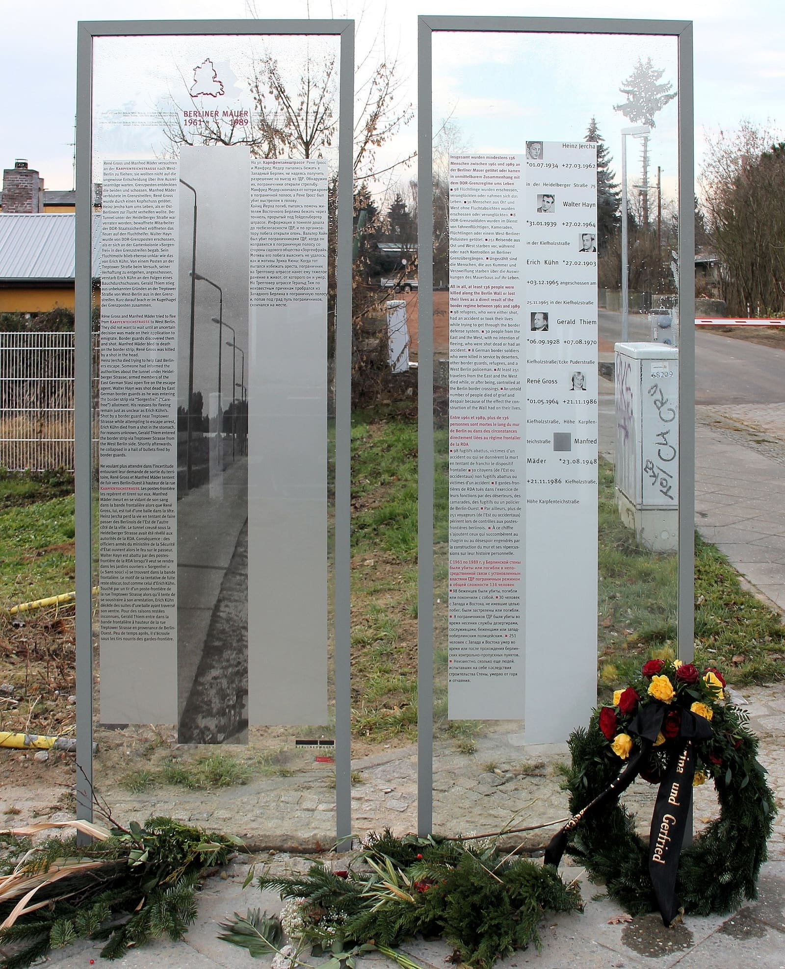 Two glass memorial steles with text and small portraits, a wreath laid at their foot.