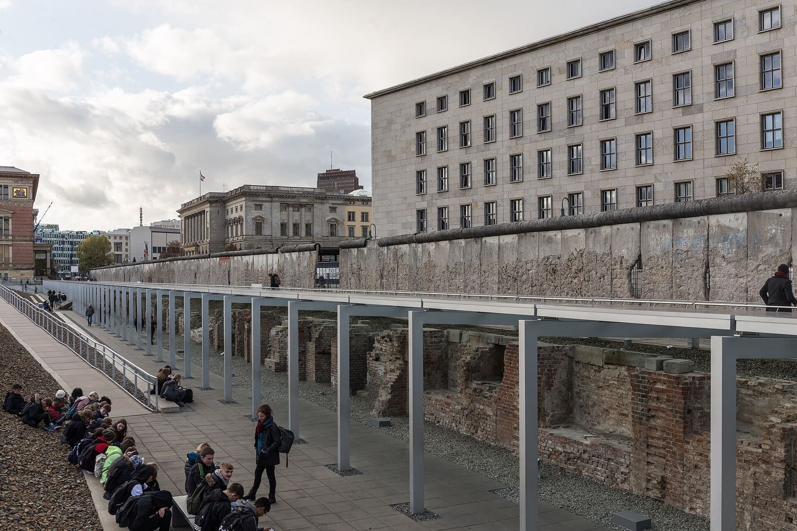 A long weathered concrete wall section in front of a large stone government building.