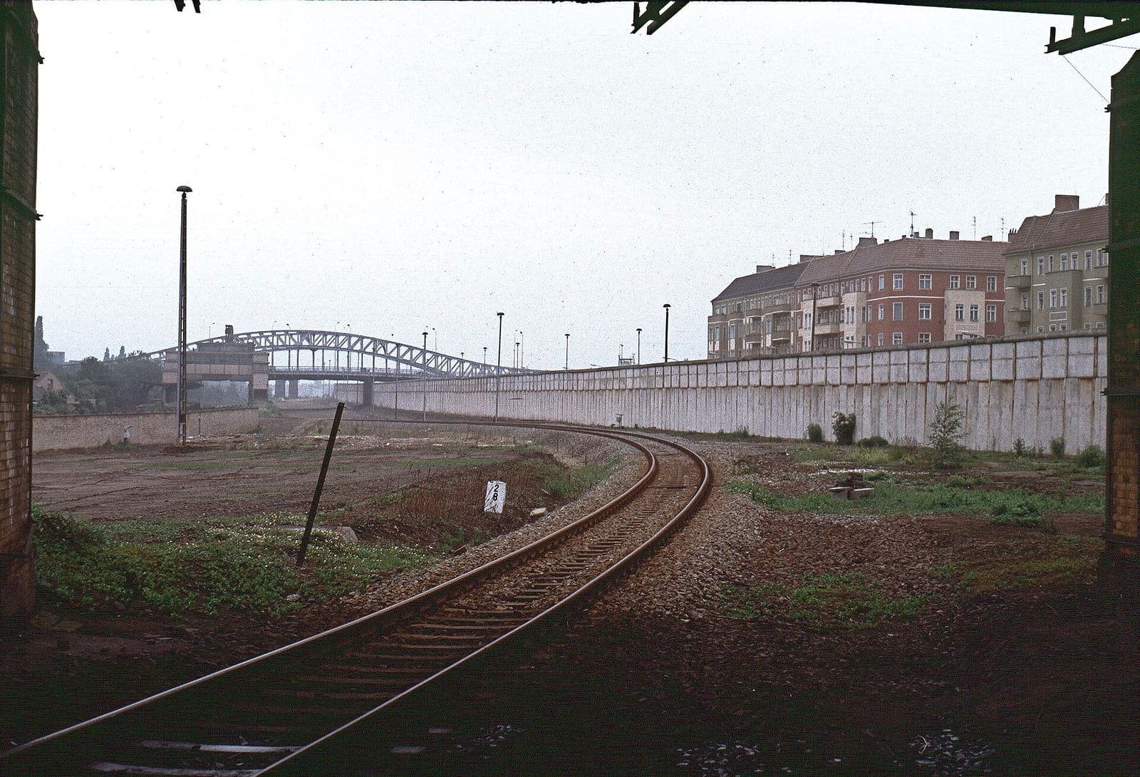 A railway cutting with tracks, a concrete wall alongside, and a steel road bridge crossing overhead