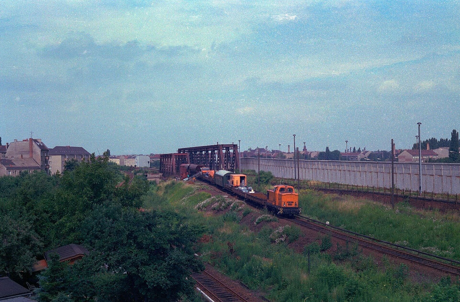 Railway land split by a long concrete wall, with West Berlin tracks on the left and East Berlin tracks on the right