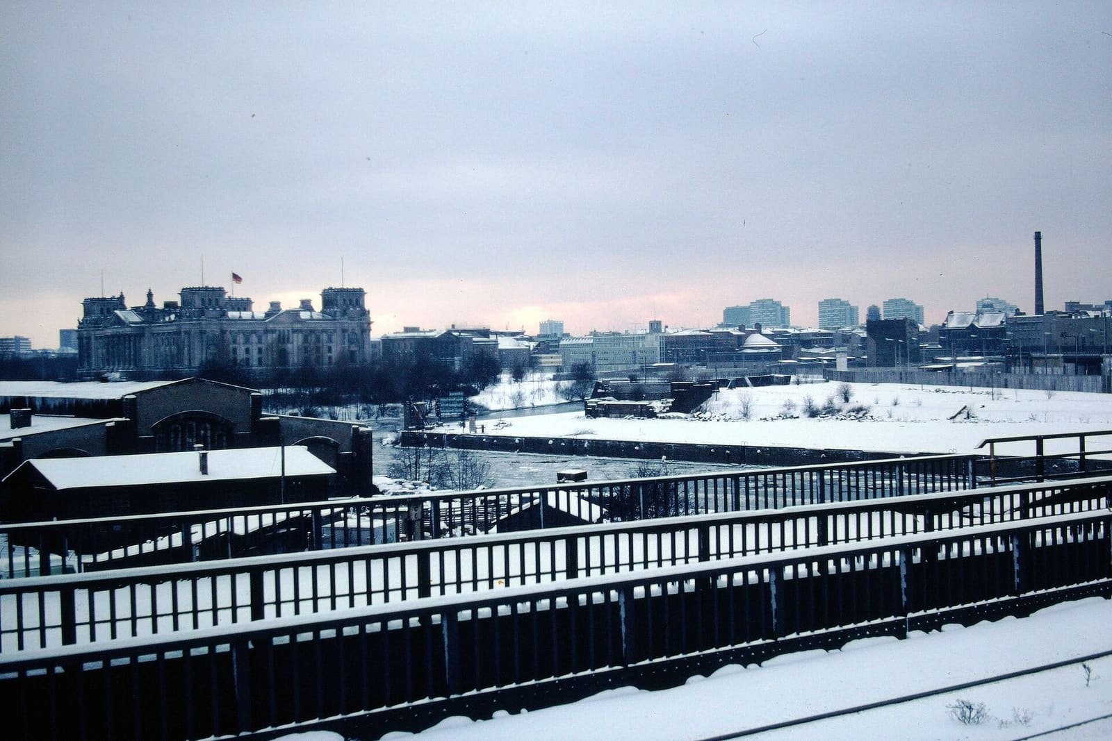 The large stone Reichstag building in winter, with border barriers visible along the river bank.
