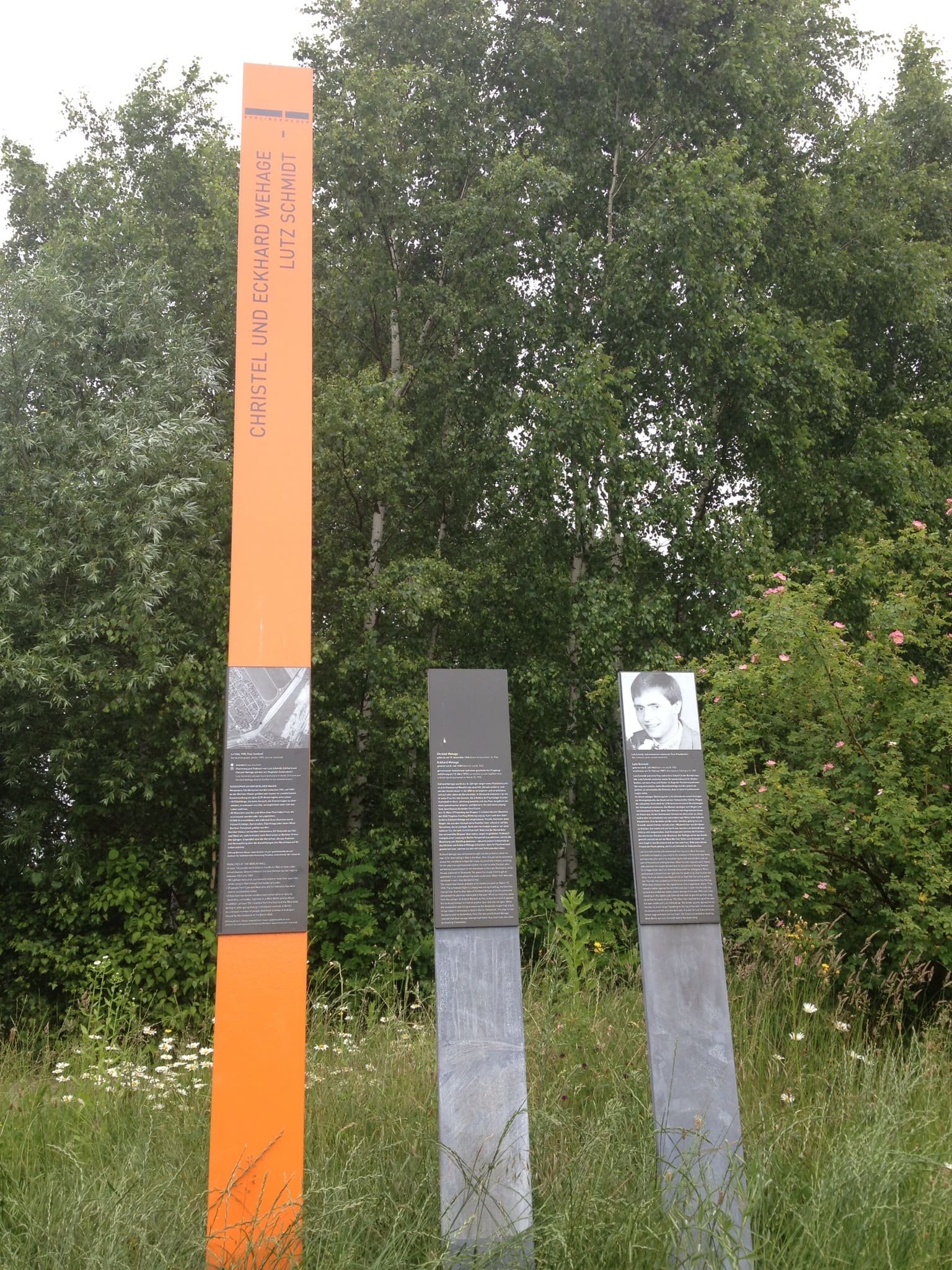 A tall rust-coloured memorial stele standing in open parkland