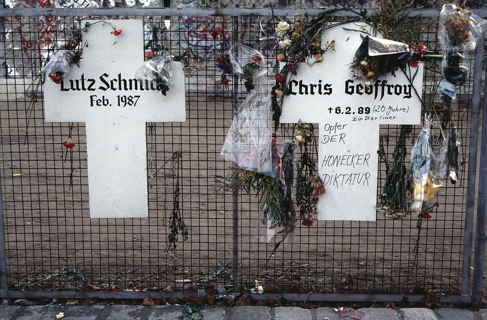 White wooden crosses bearing names, fixed in front of the Berlin Wall