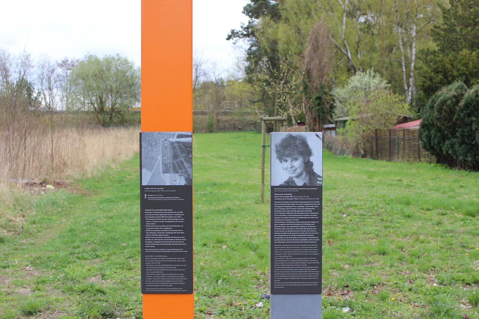 A rust-coloured memorial stele with a portrait and text, standing among trees
