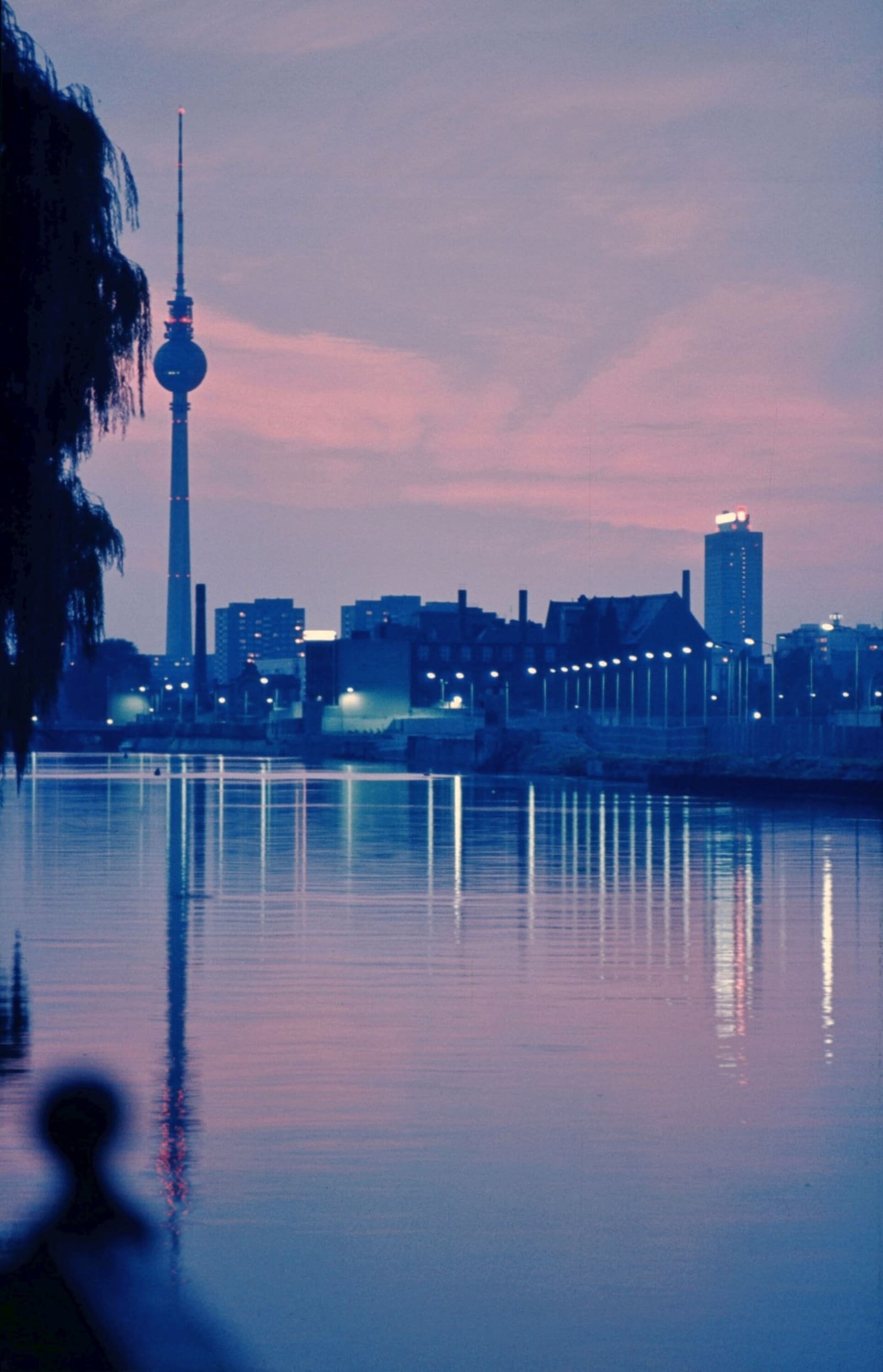 Night view across the river Spree from the Kreuzberg bank towards a brightly floodlit strip of wall on the far shore.