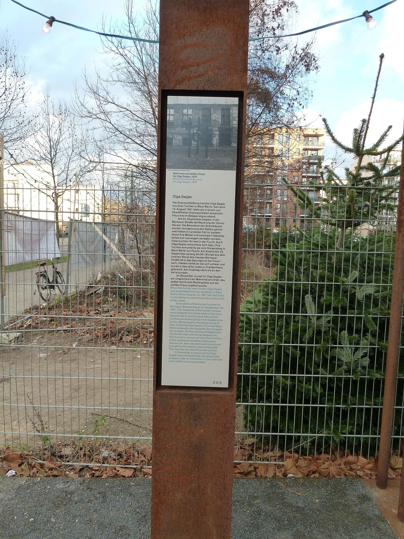 An upright memorial stele with text on the pavement of Bernauer Straße.