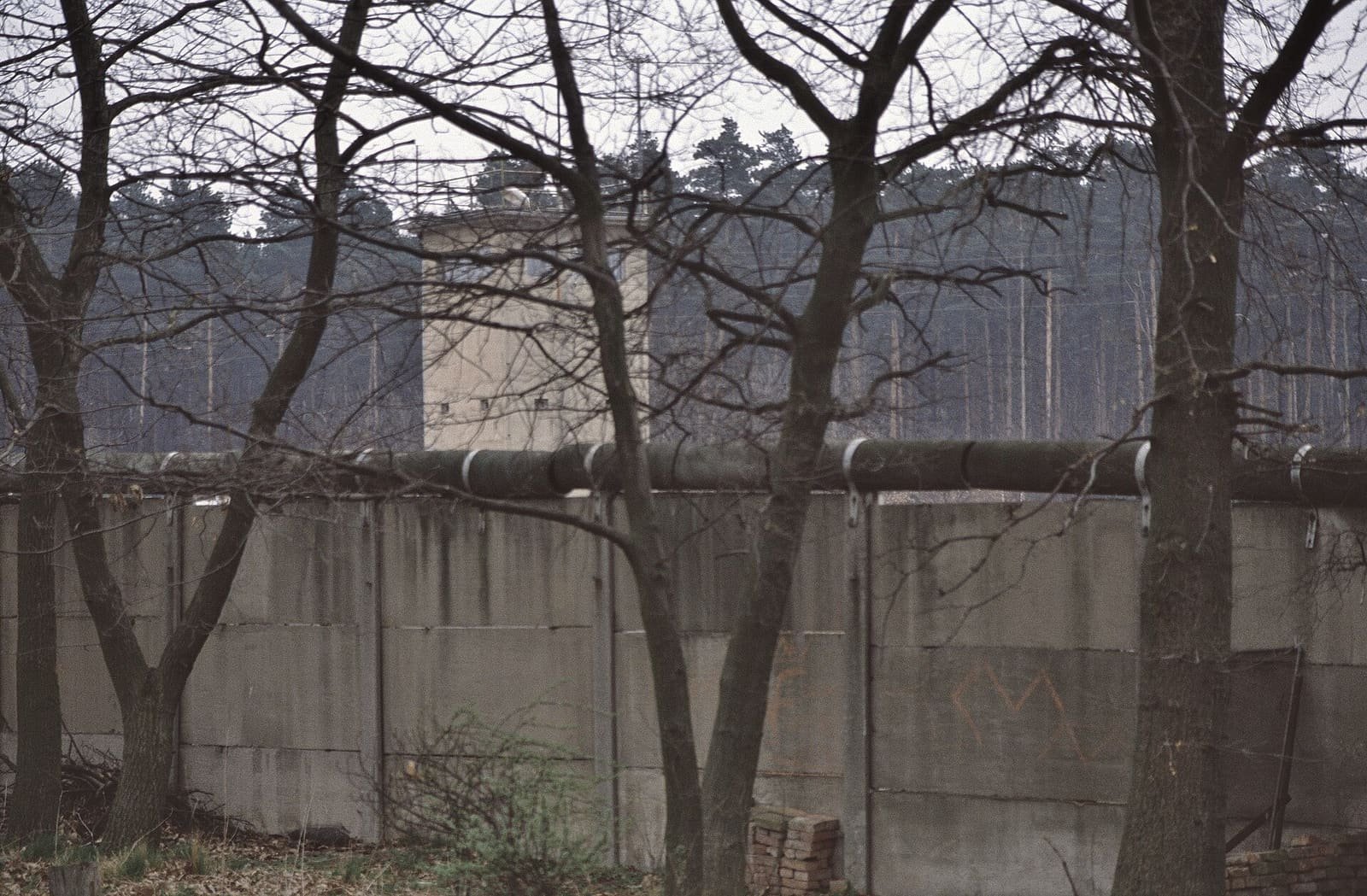 A tall concrete watchtower behind the Berlin Wall among trees